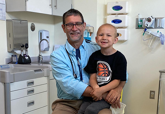 Bald boy sitting on the lap of a doctor in the exam room